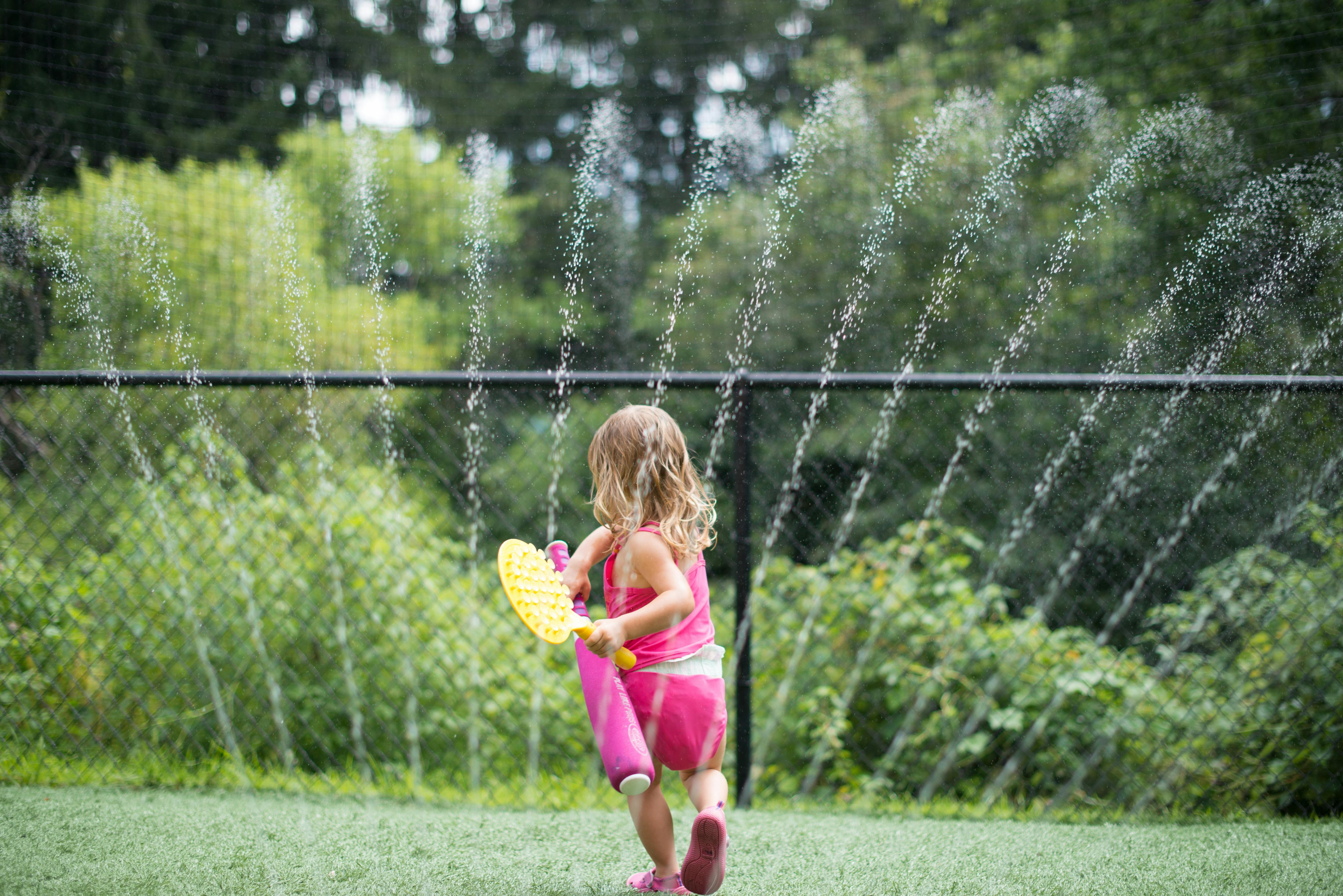 Child playing with a toy in front of a sprinkler