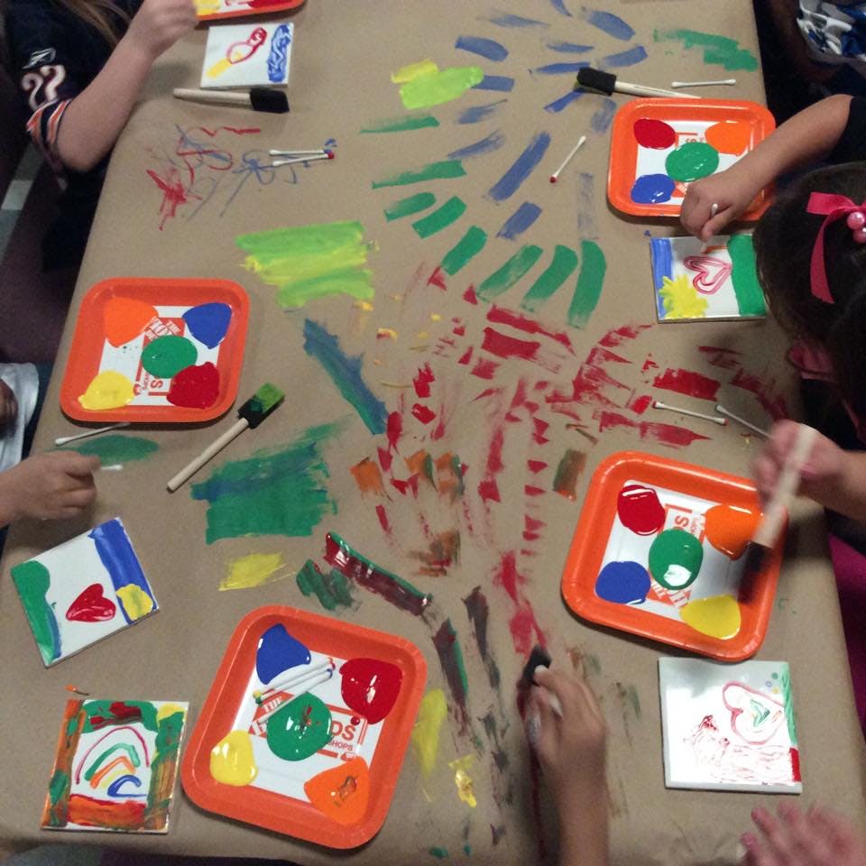 Children painting on a table covered with paper and paint and art supplies