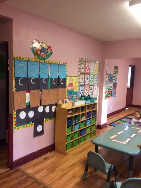 Classroom with child at a table, shelves with bins, and learning materials on wall