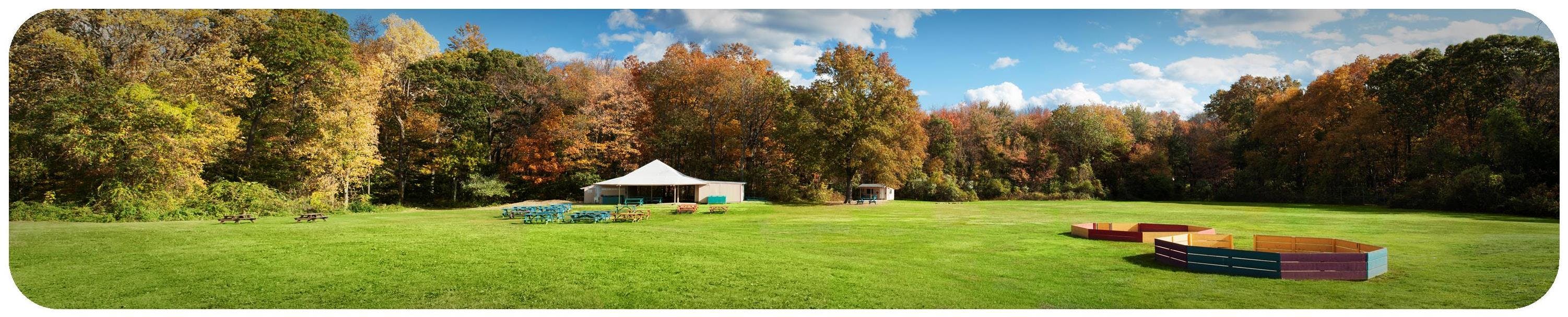 Field with a tent, picnic tables, and wooden borders under a blue sky