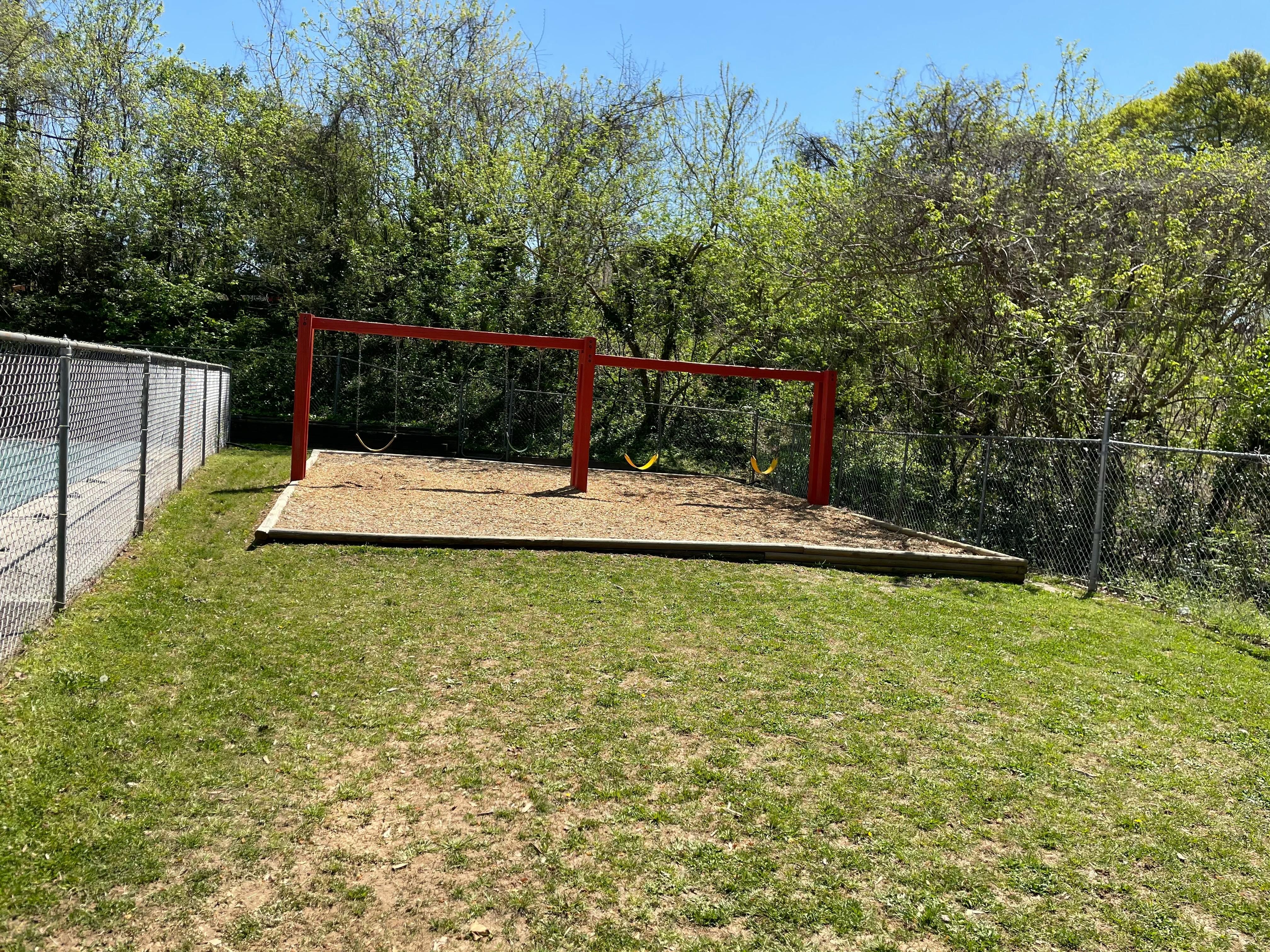 Empty swing set on a patch of sand surrounded by grass and trees