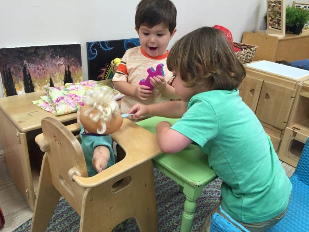 Two children playing with a doll in a high chair at a table