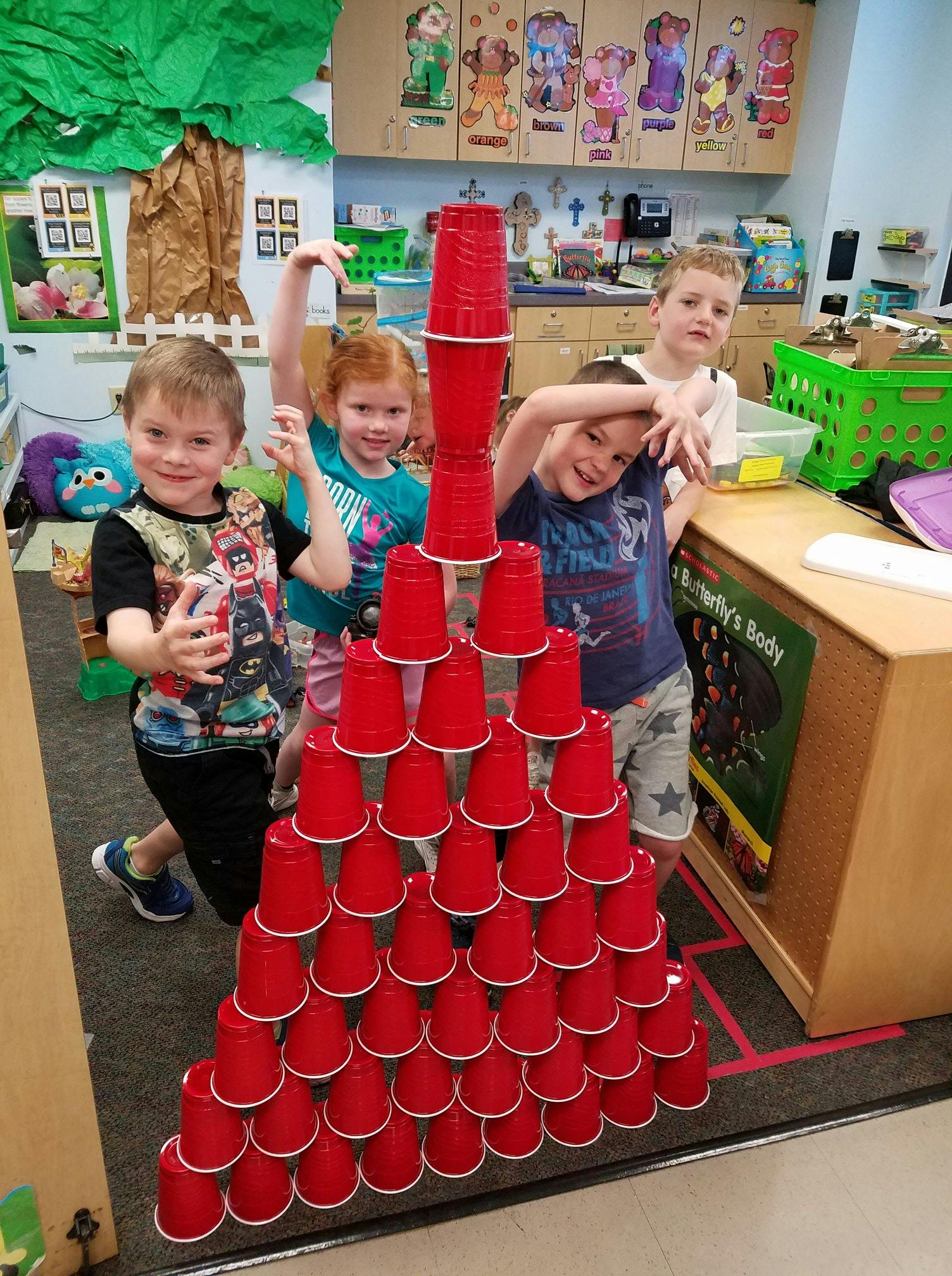 Four children standing around a large pyramid of red plastic cups
