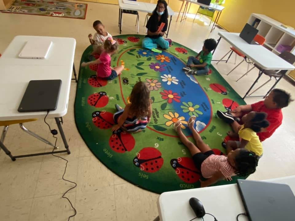 Children and an adult sitting on a colorful rug in a classroom