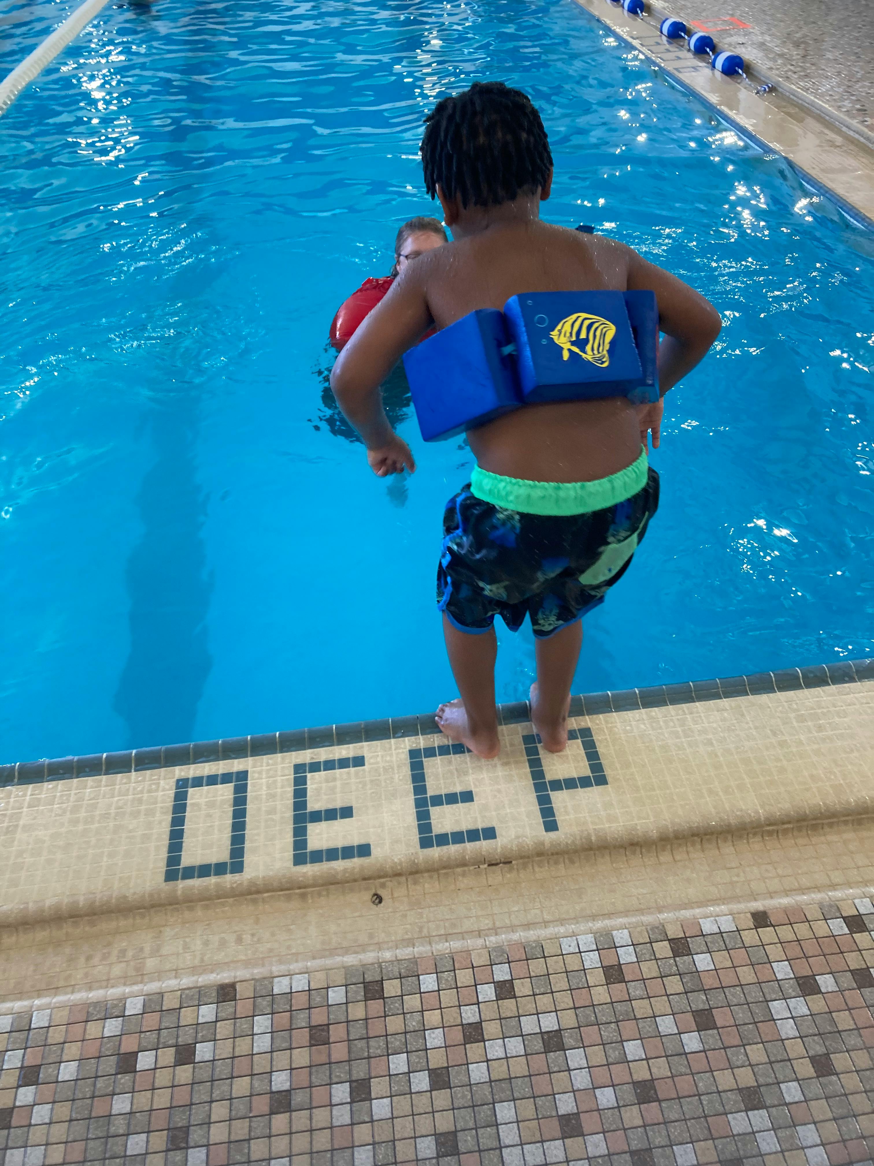 Child with a blue swim float standing at the edge of a swimming pool