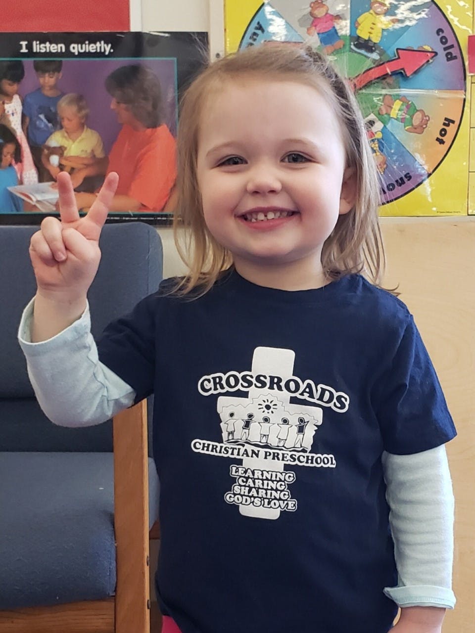 Child making a peace sign, wearing a Crossroads Christian Preschool shirt