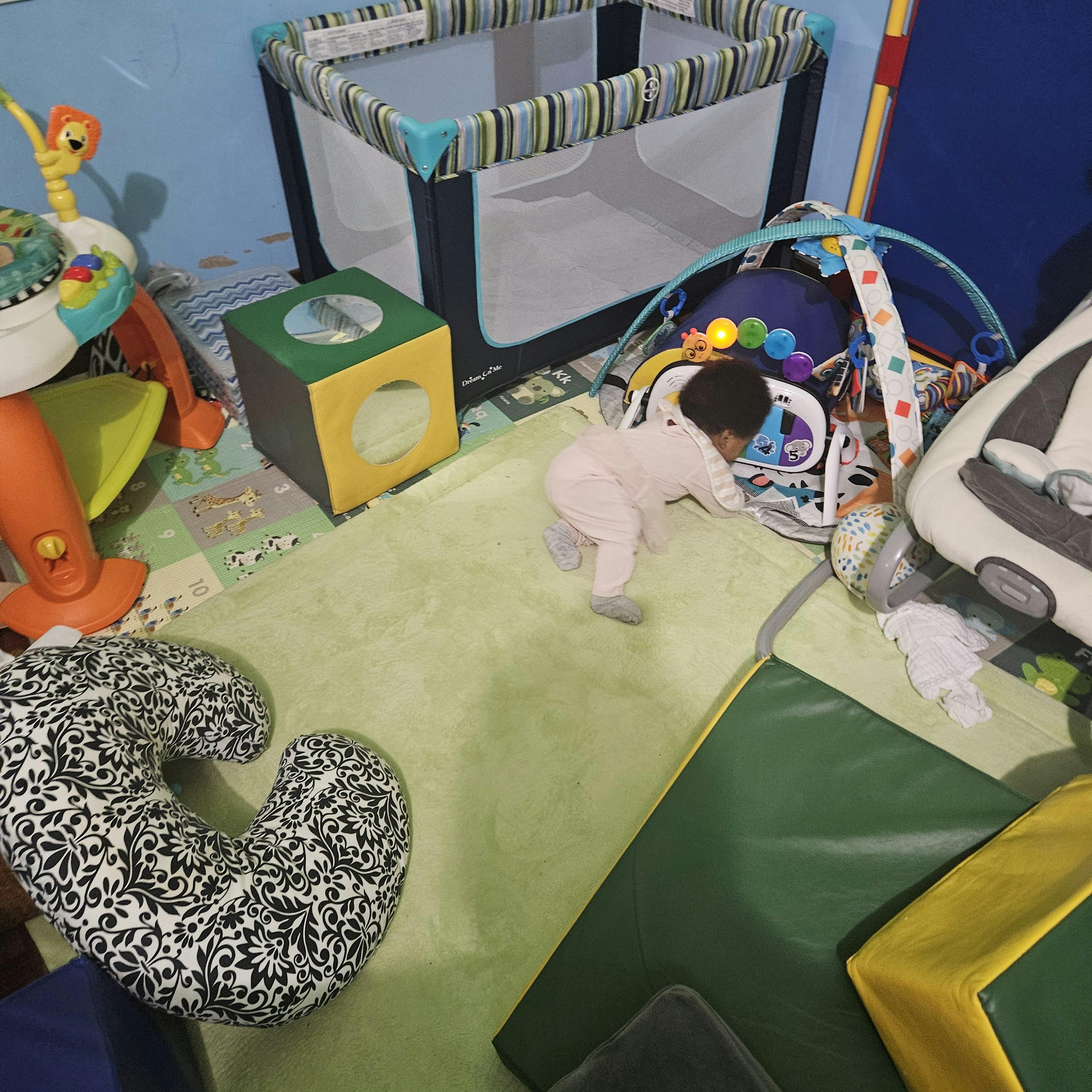 Child crawling on a green mat toward a play gym