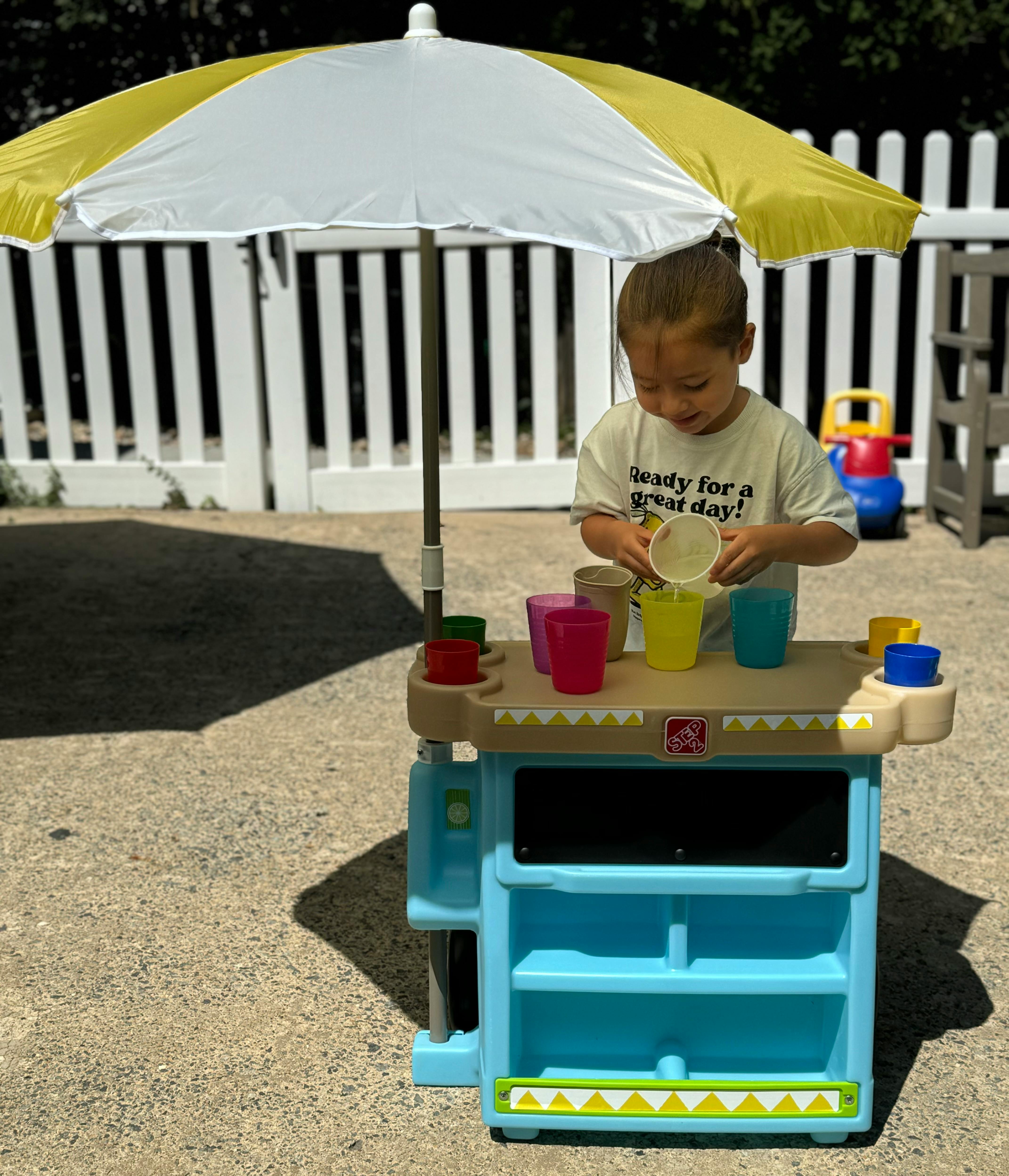Child playing with cups at a toy stand under an umbrella