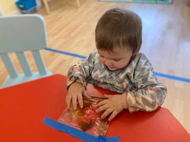 Child playing with a sensory bag on a red table