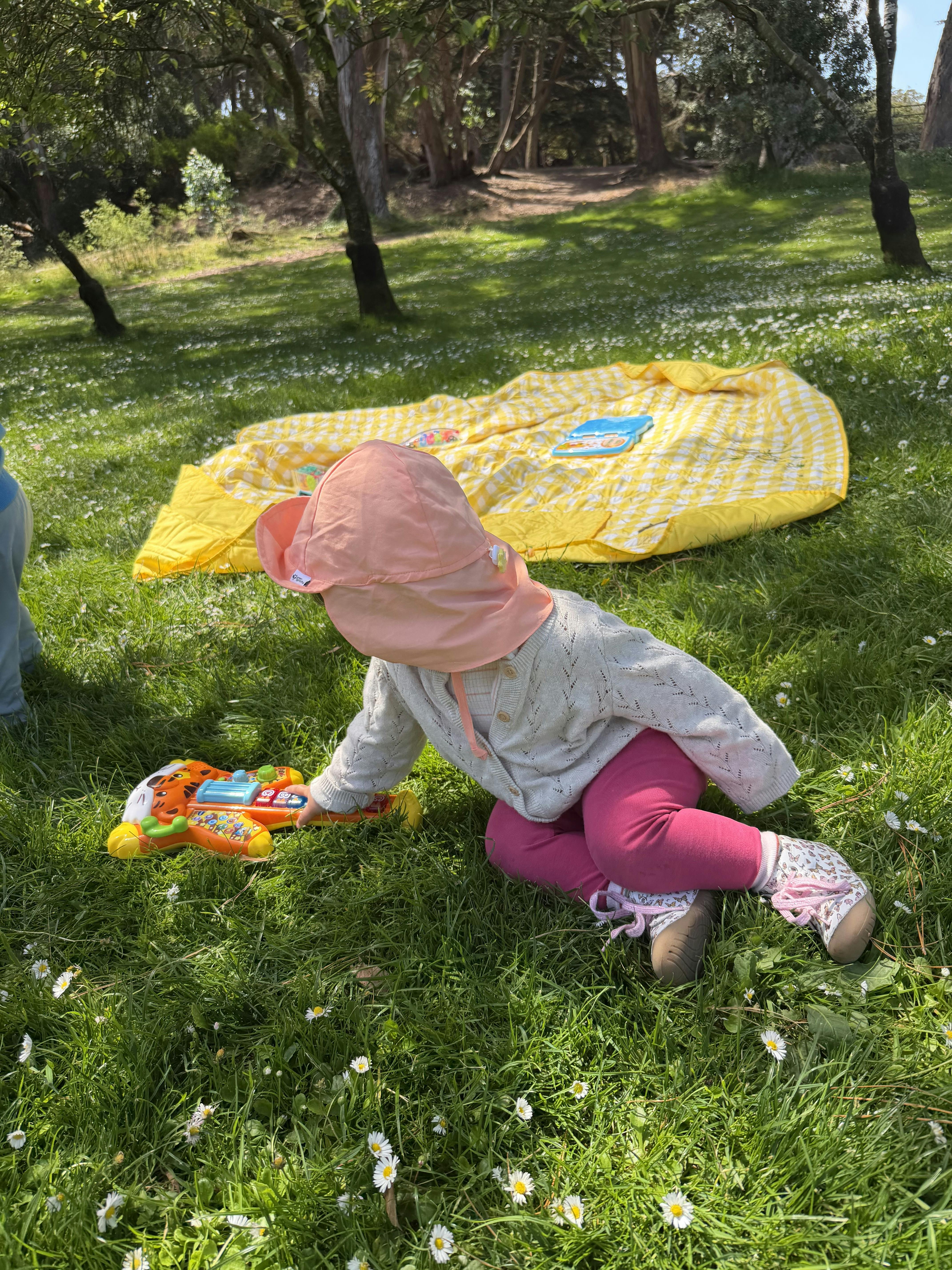 Child in a sun hat sitting on grass playing with a toy