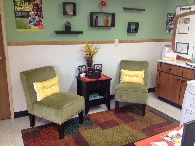 Two green chairs with yellow pillows and a side table on a patterned rug