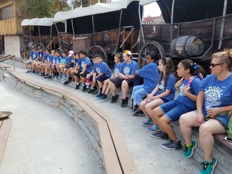 Group of children and adults sitting on a bench in front of wagons