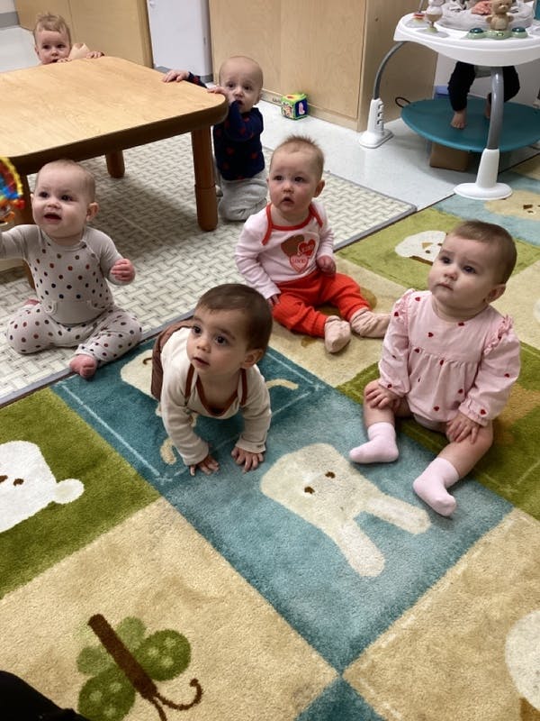 Multiple babies on a patterned rug, some sitting, one crawling