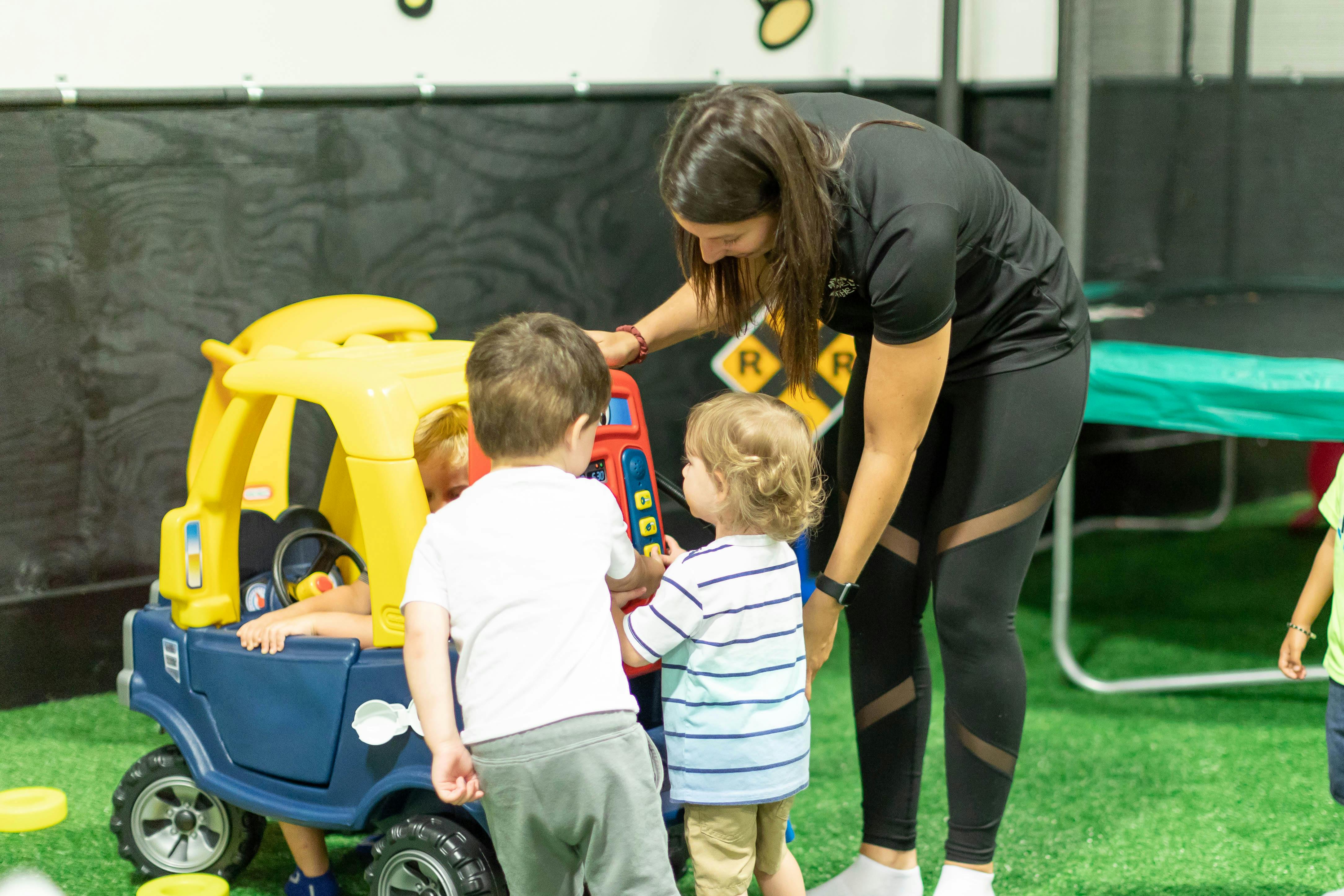 Adult supervising three children playing with a toy car