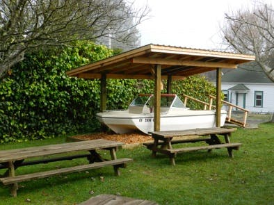 Boat under a wooden shelter with picnic tables in the foreground
