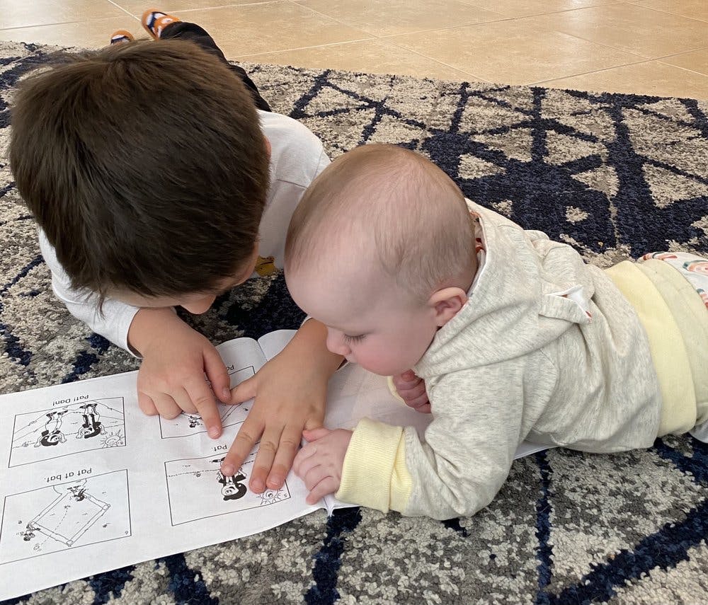 Child and baby on floor looking at a paper with diagrams