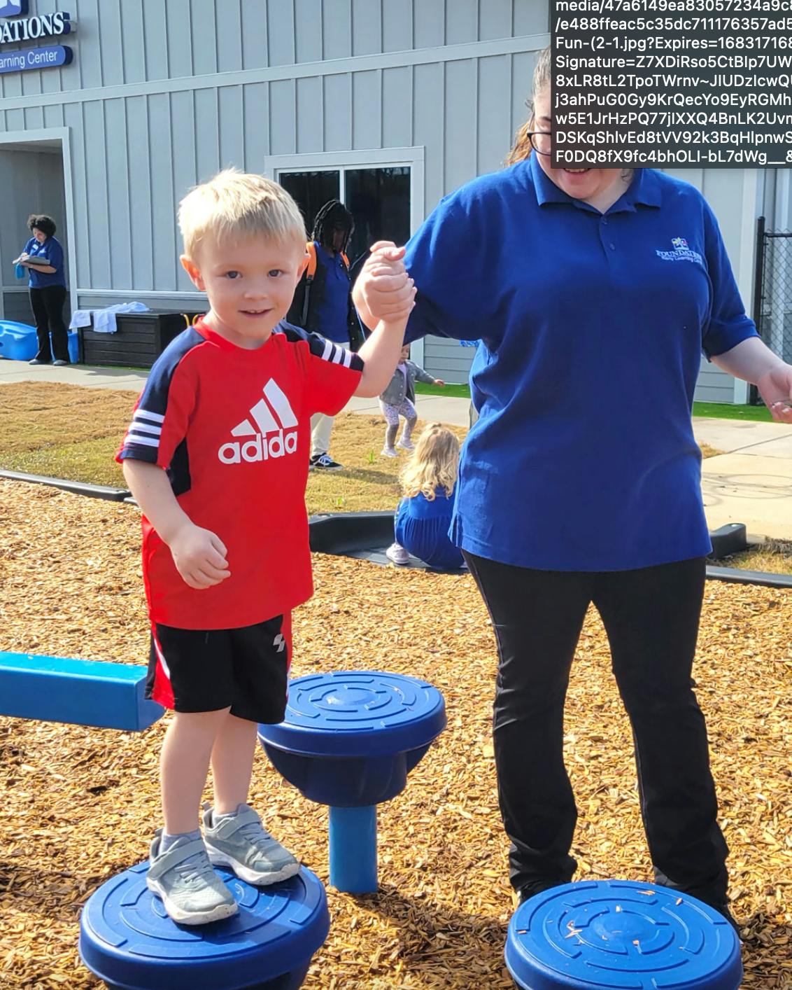 Child in red shirt holding hands with an adult on a playground