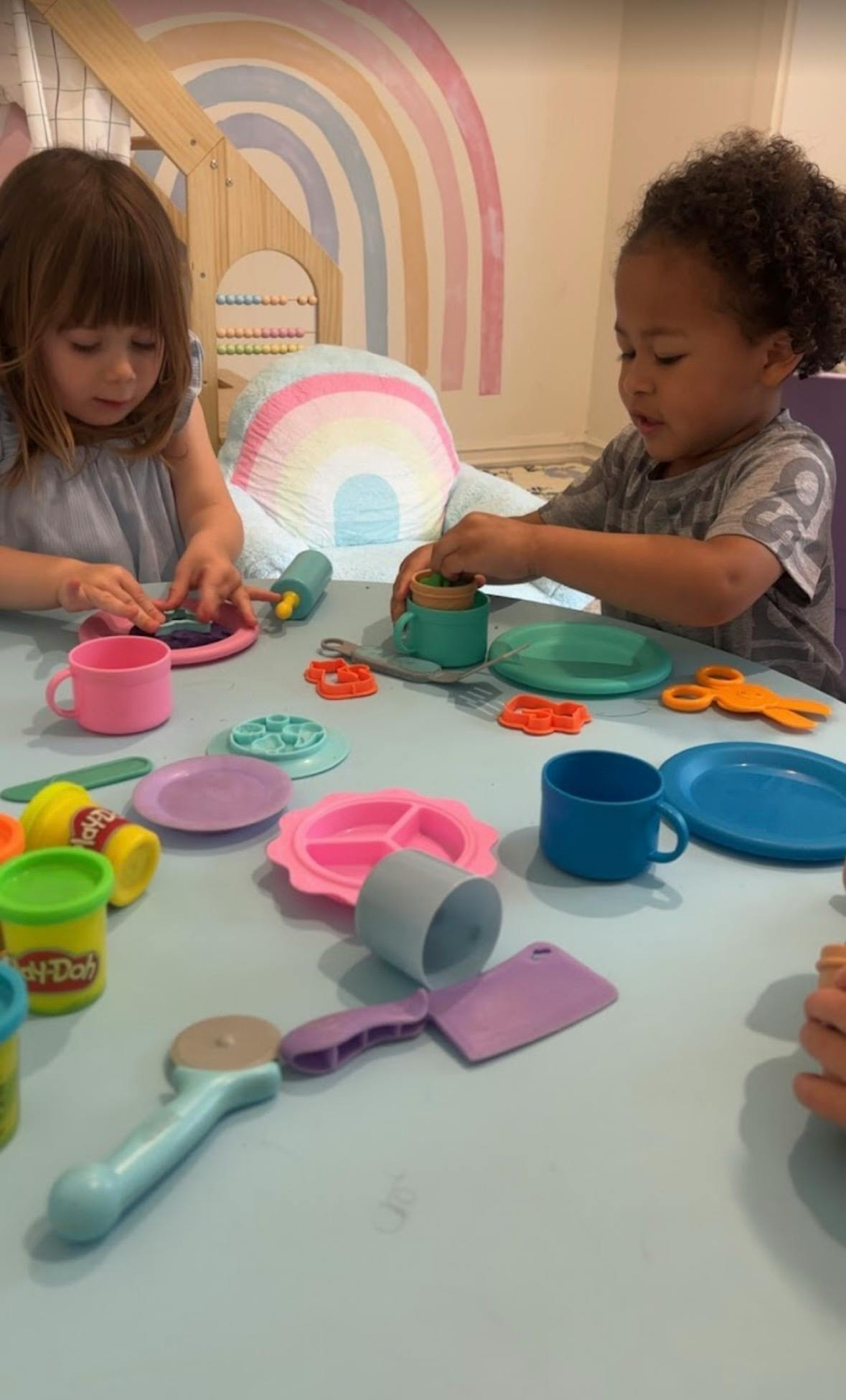 Two children playing with colorful Play-Doh and toy dishes