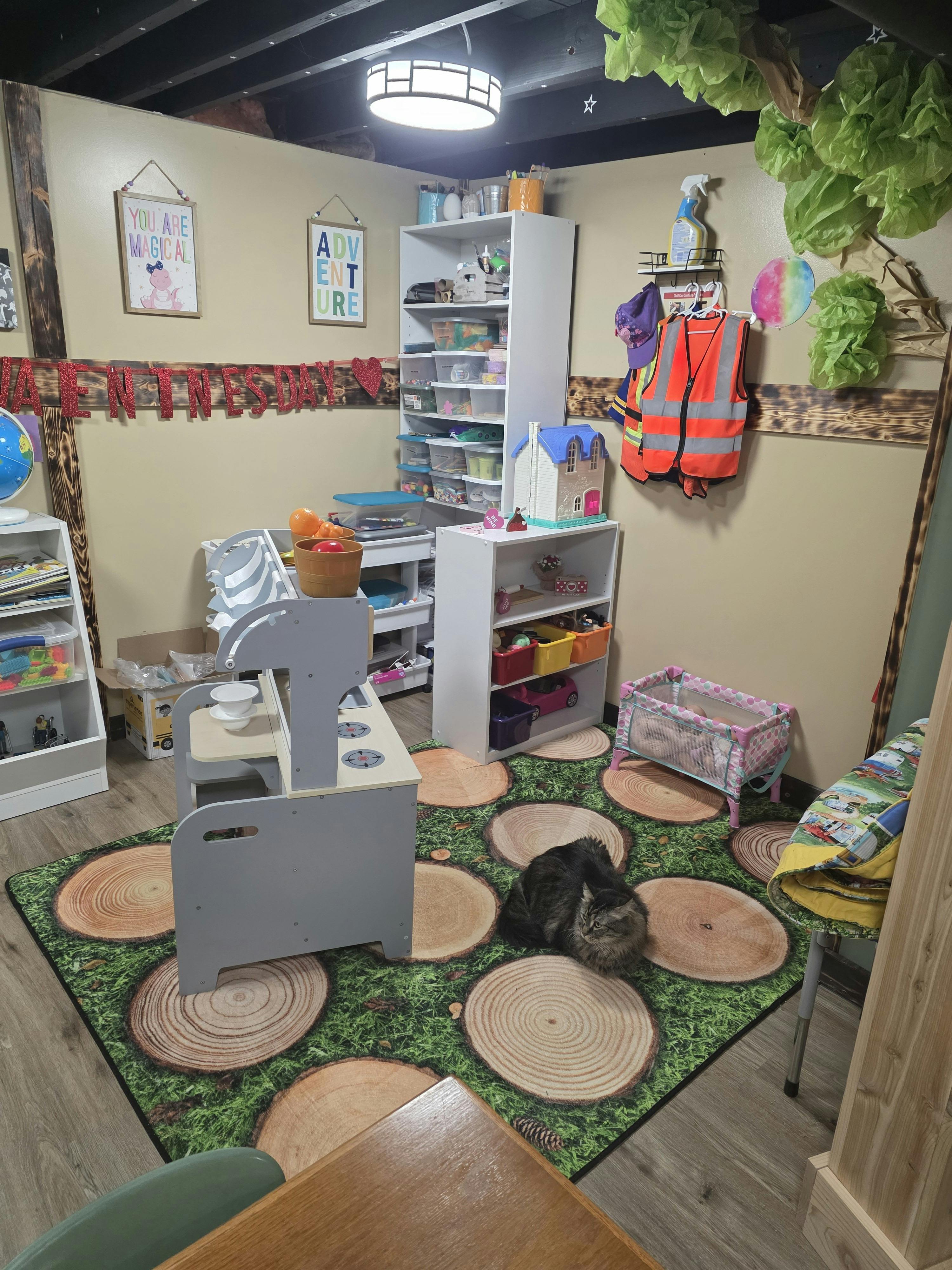 A cat on a rug that looks like grass and tree stumps in a playroom with toys