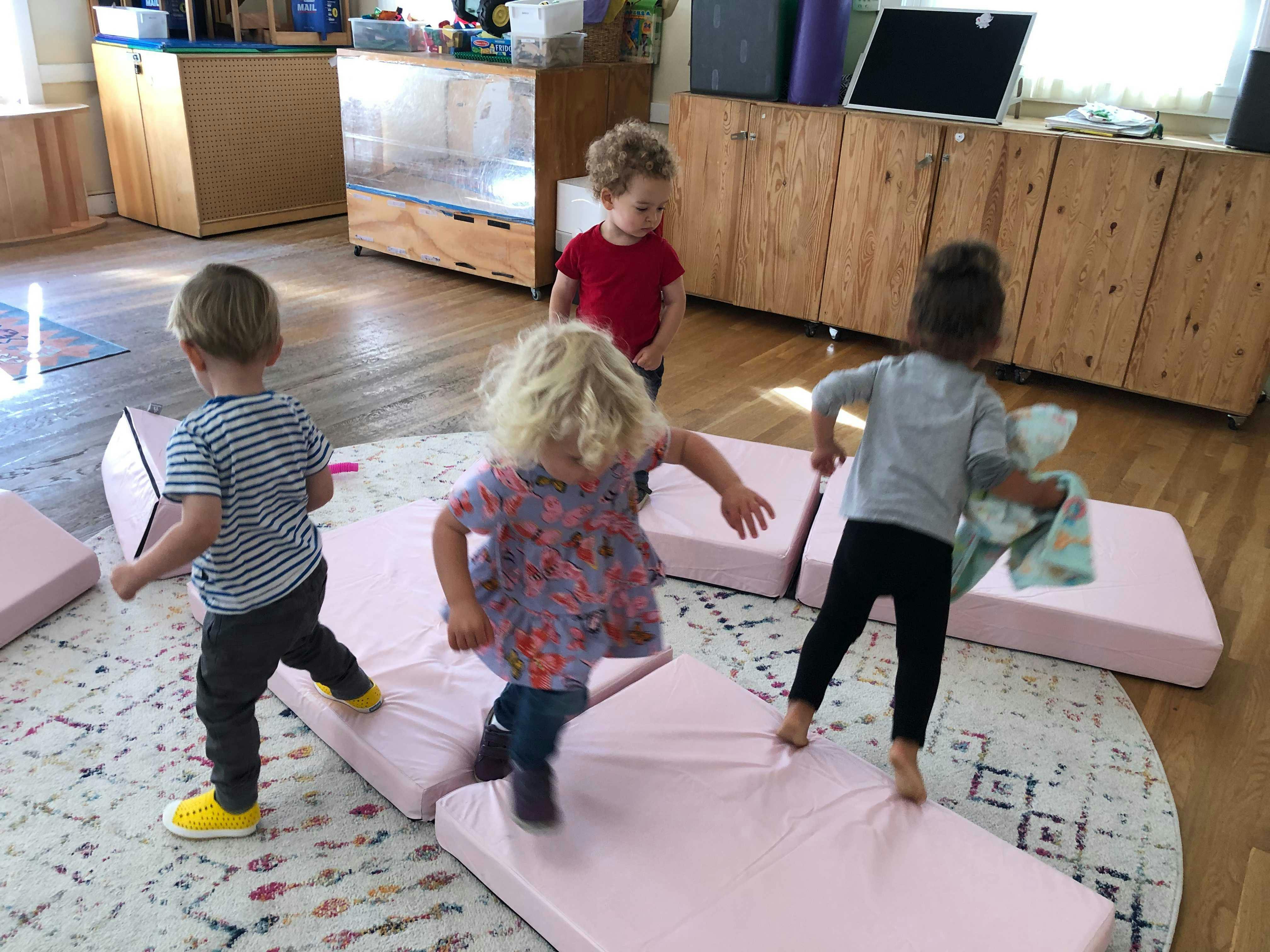 Four children playing on pink mats in a room