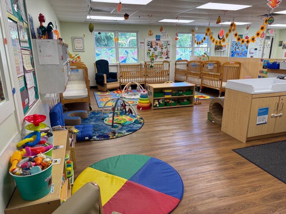 An empty nursery room with multiple cribs, a changing table, and play mats