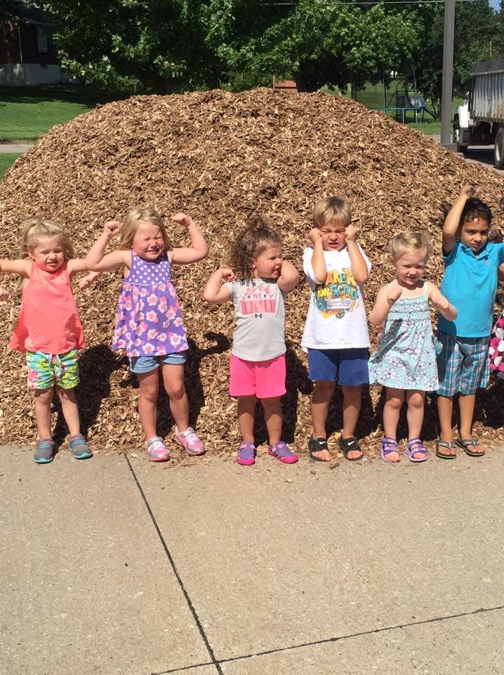 Six children standing in front of a pile of wood chips