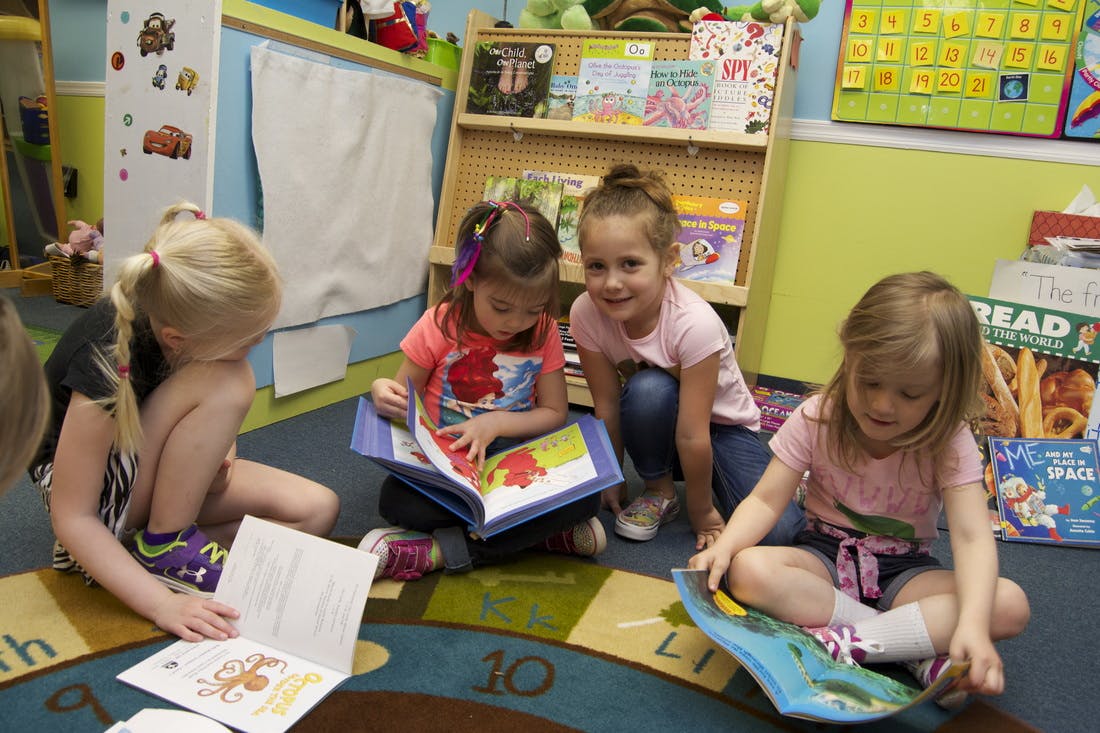 Four children reading books on a classroom floor