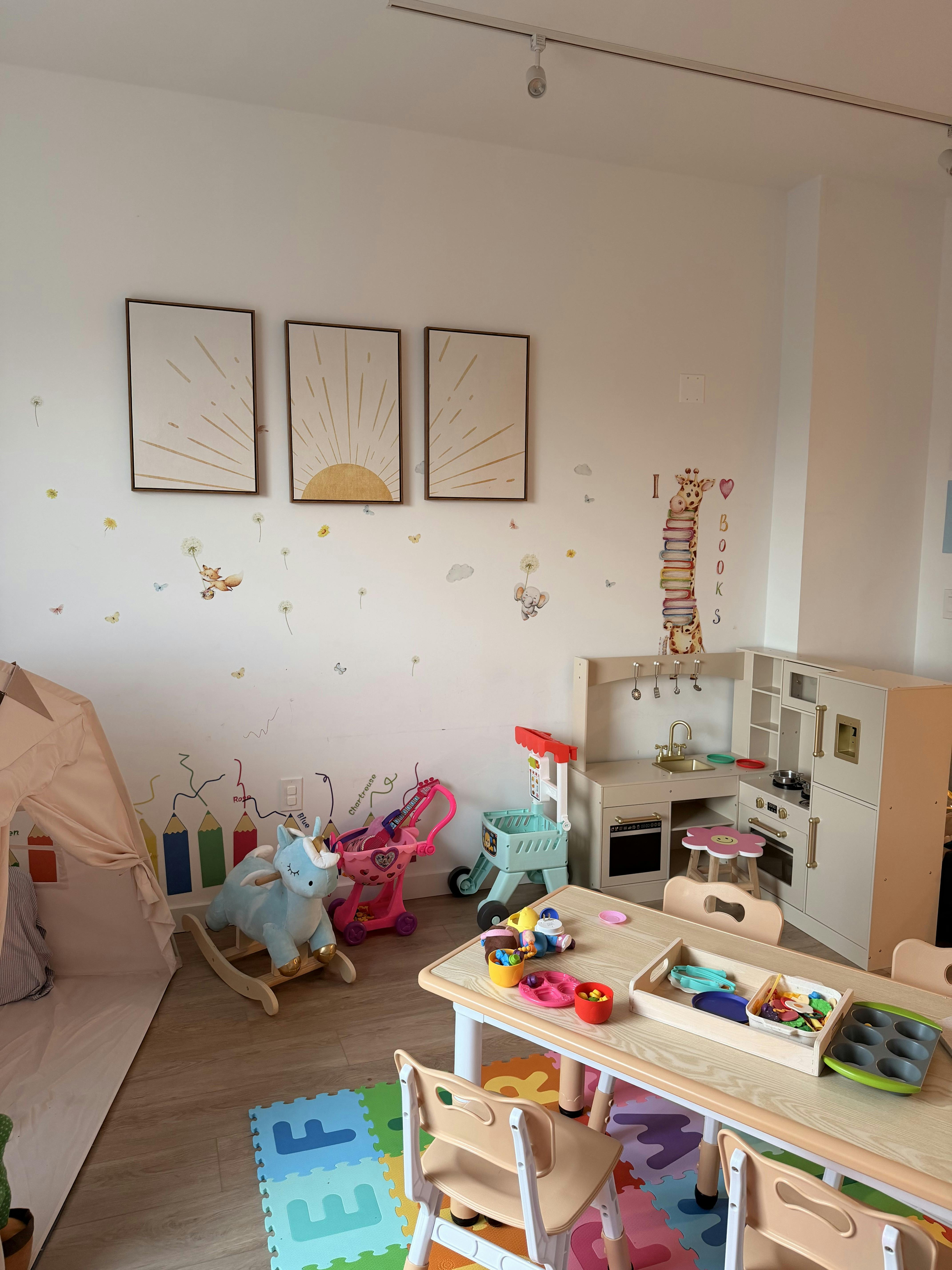 Children's play area with a toy kitchen, unicorn rocker, and table with chairs