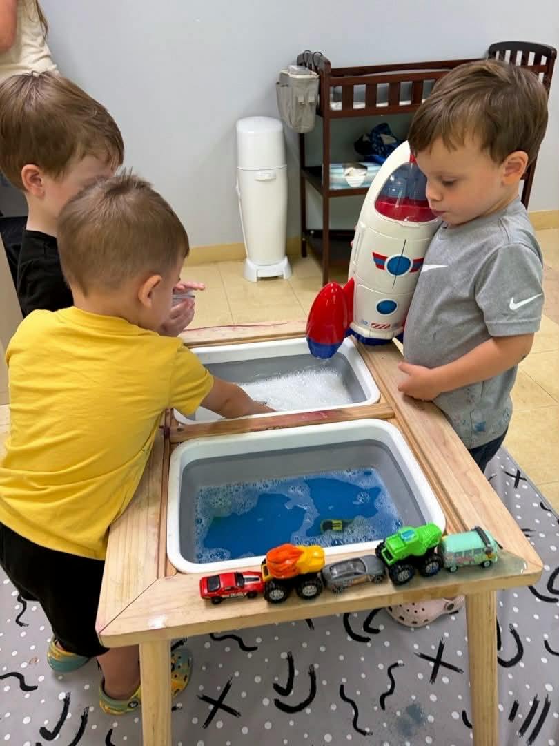 Three children playing with water and toy vehicles at a sensory table