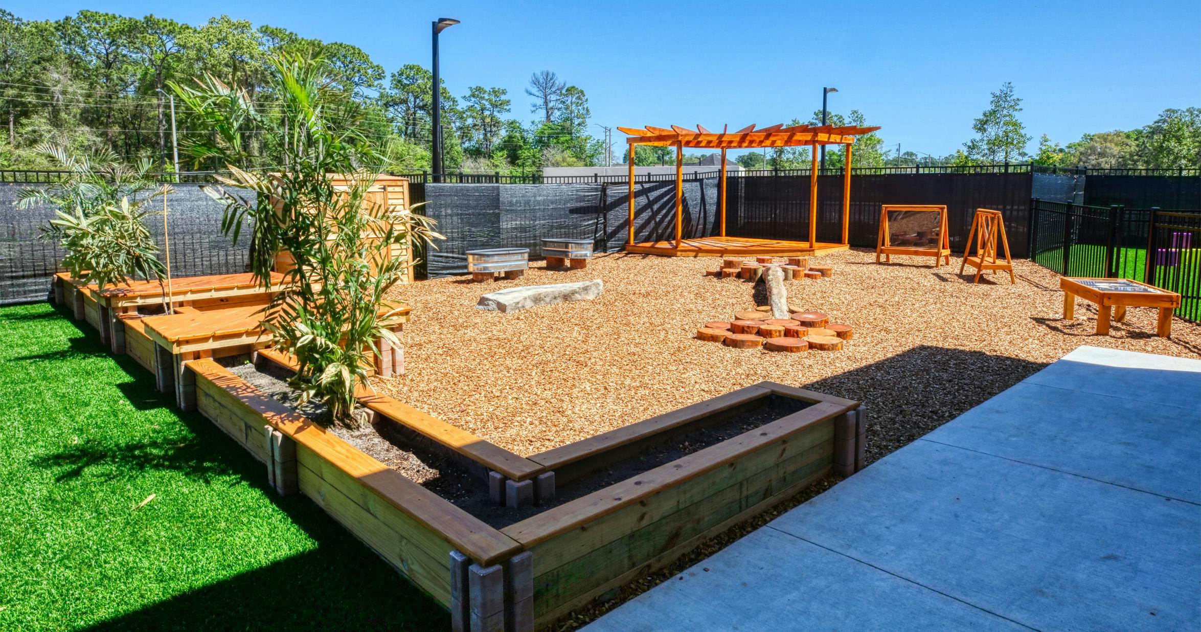 An outdoor play area with artificial turf, wood chip ground cover, and wooden play structures