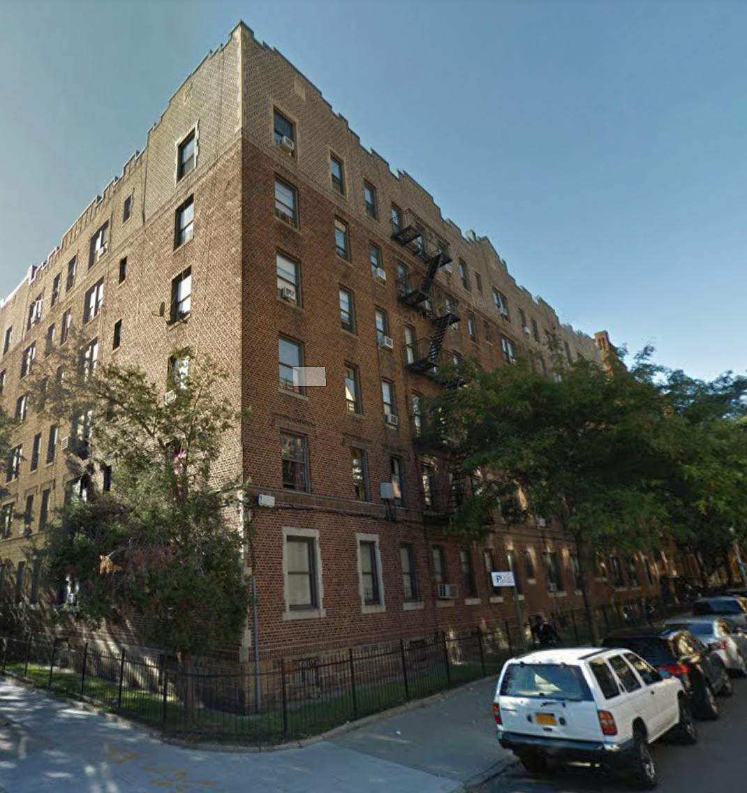 Large brick apartment building with fire escapes and parked cars on the street