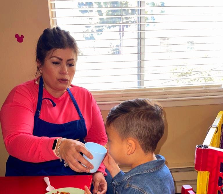 Person in apron holding a cup for a child