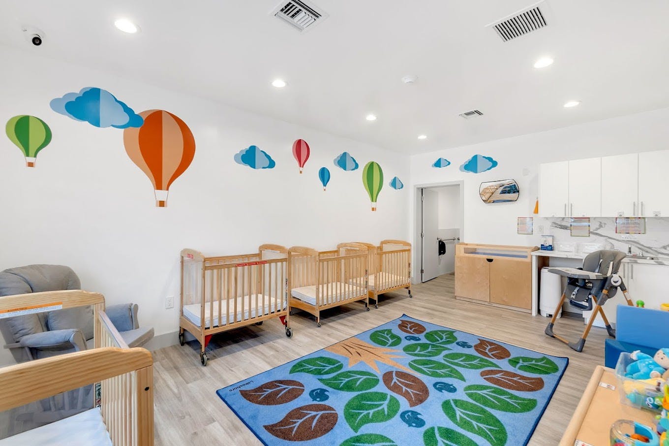 Nursery room with multiple cribs, a rug, and hot air balloon wall decals