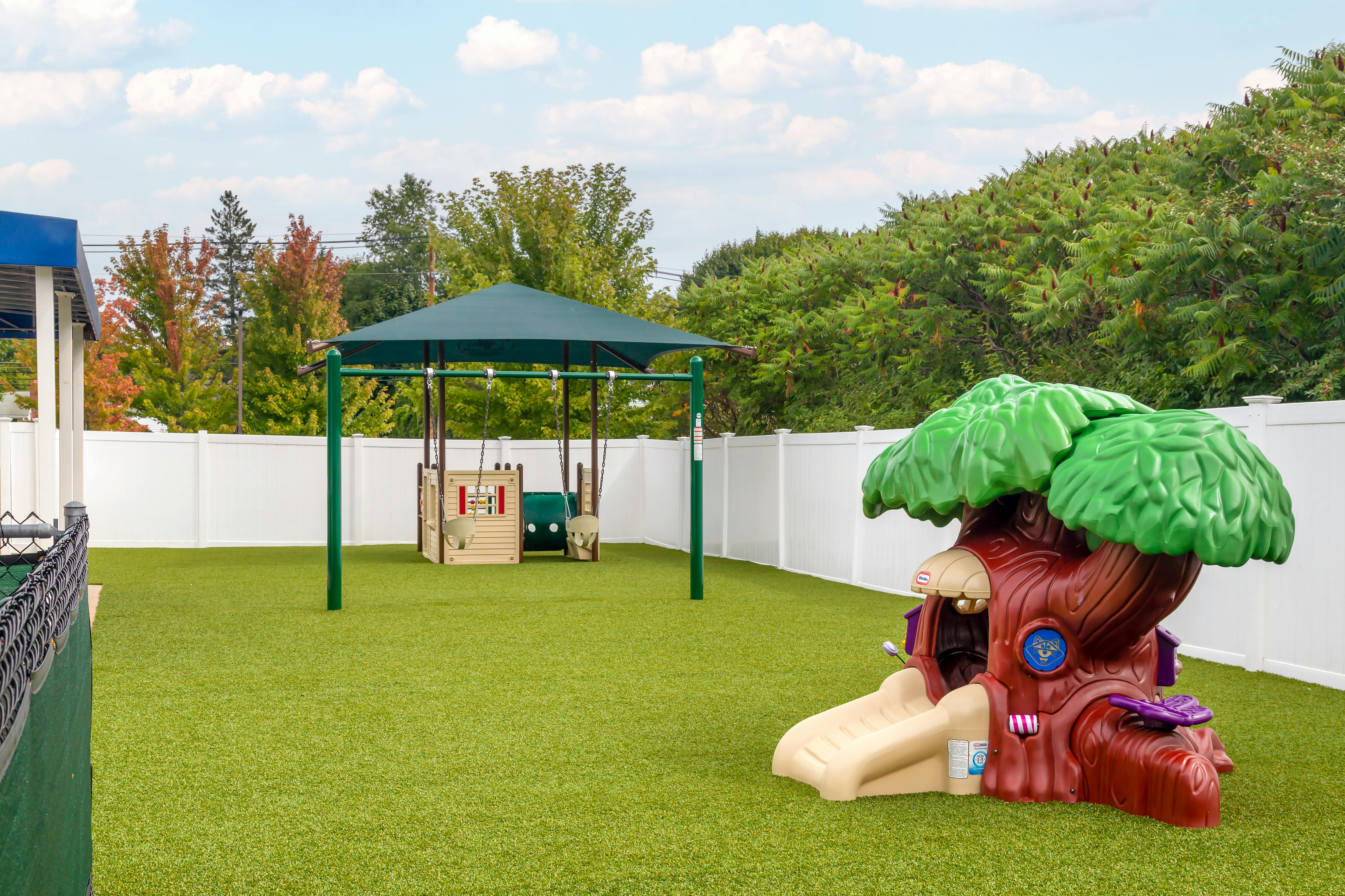 Playground with swings, a playhouse, and a tree-shaped slide on artificial turf
