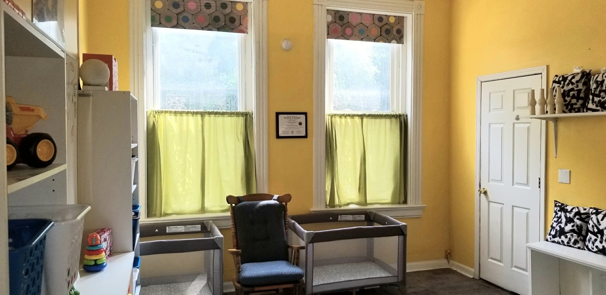 Room with yellow walls, two windows, a chair, and a white door