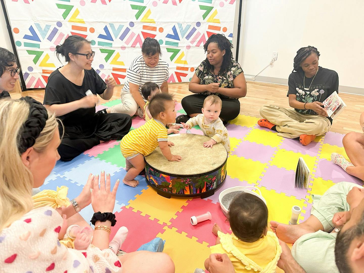 Adults and children sitting on a colorful mat around a drum