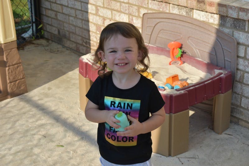 Child holding a toy, standing next to a sandbox