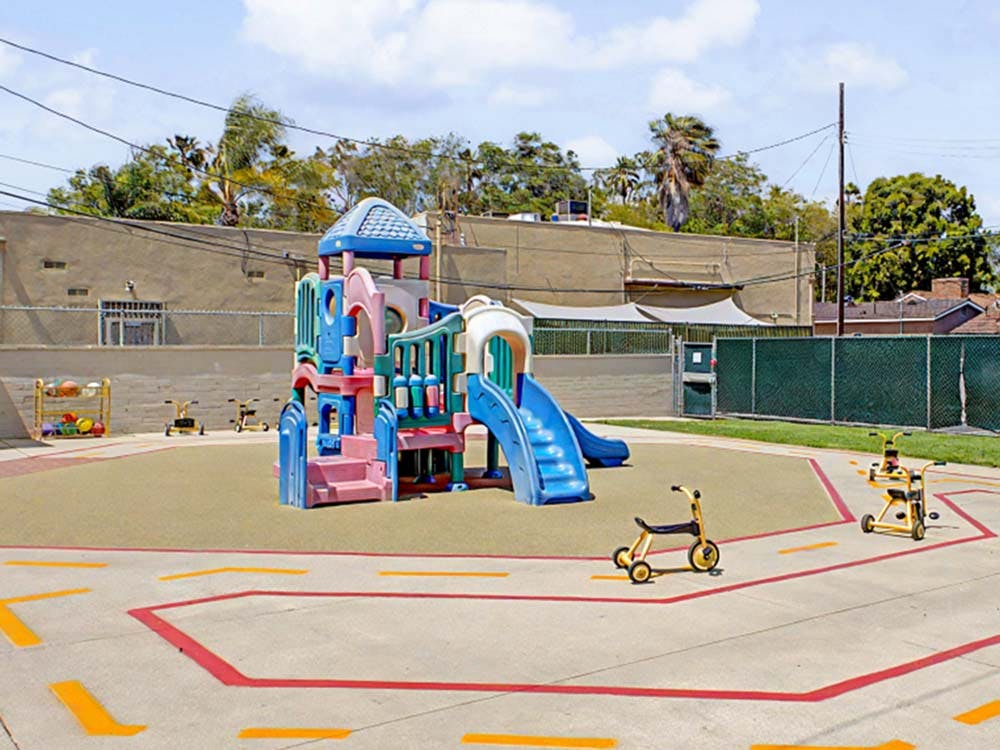 Playground with a colorful play structure, slide, and tricycles on paved ground