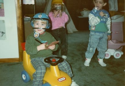 Child in helmet on toy car, two other children in background