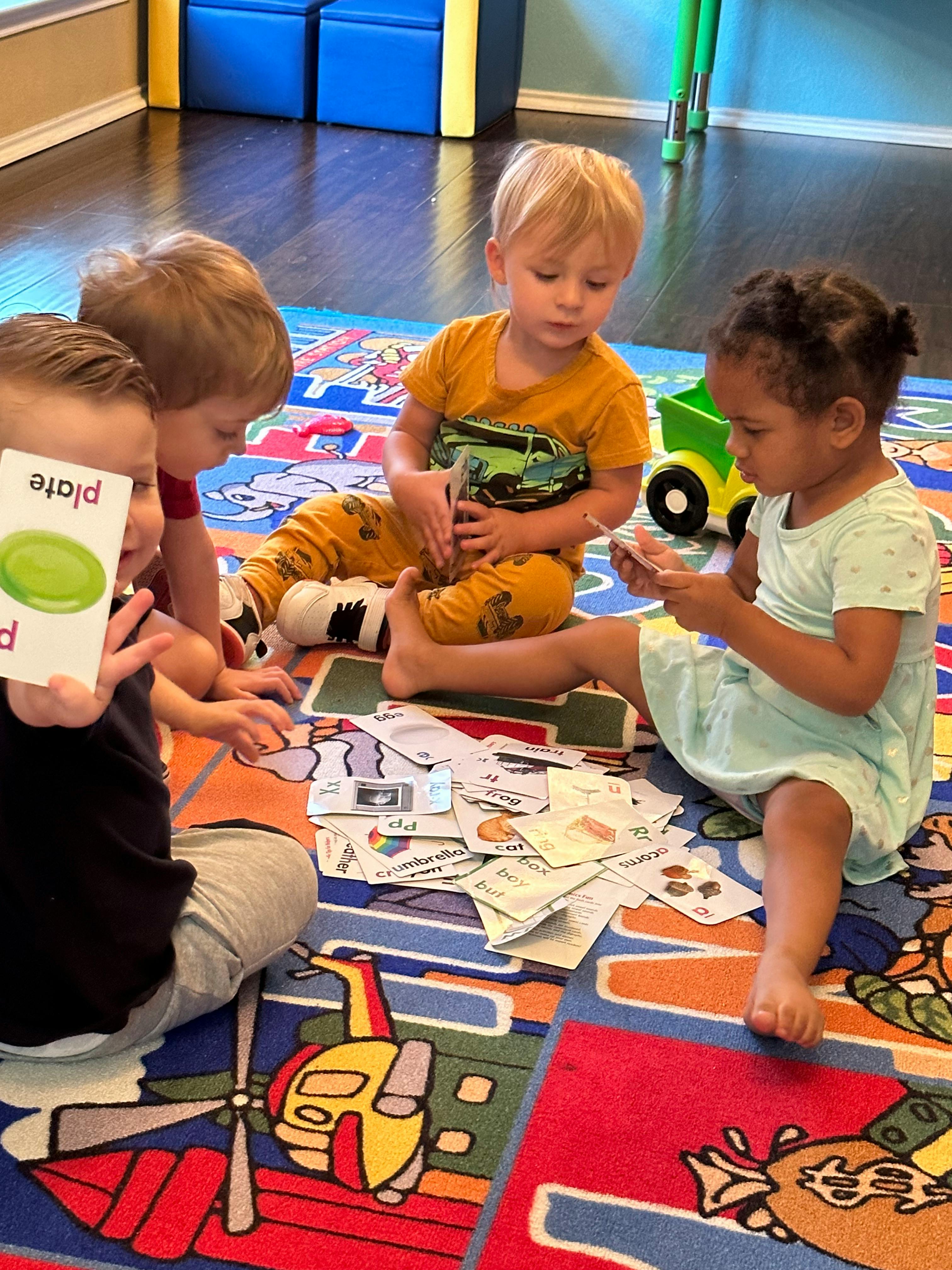 Four children sitting on a colorful rug, looking at flashcards