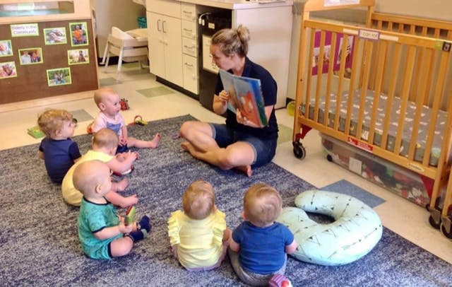 Person reading a book to a group of children in a room