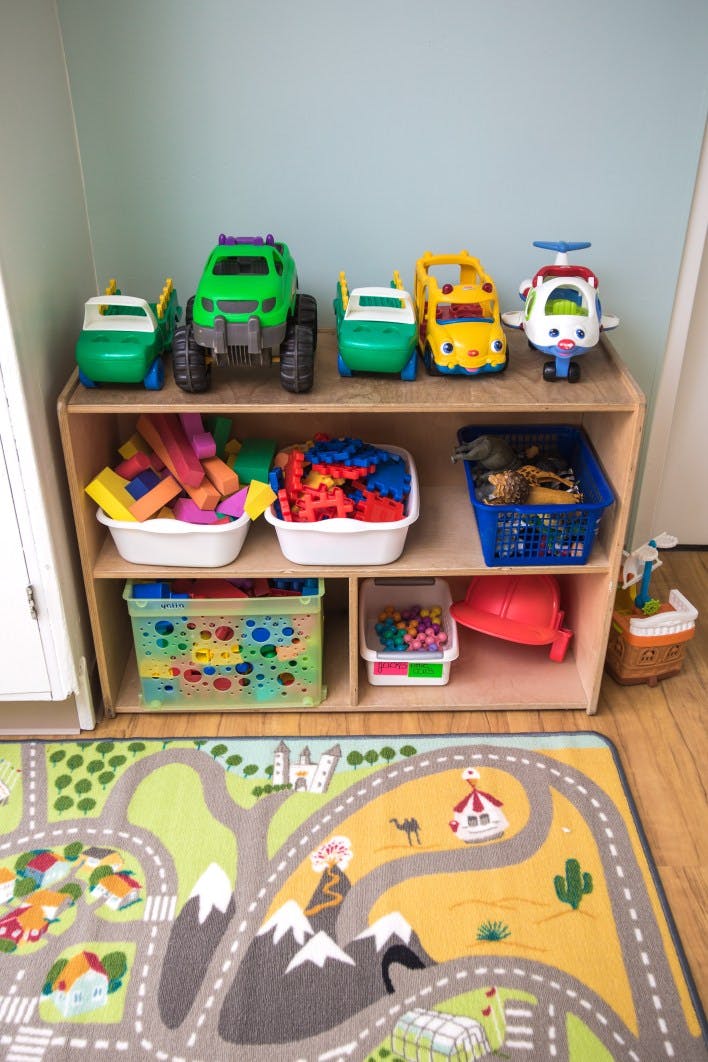 Toy shelf with toy cars, blocks, and other toys, with a play rug on the floor