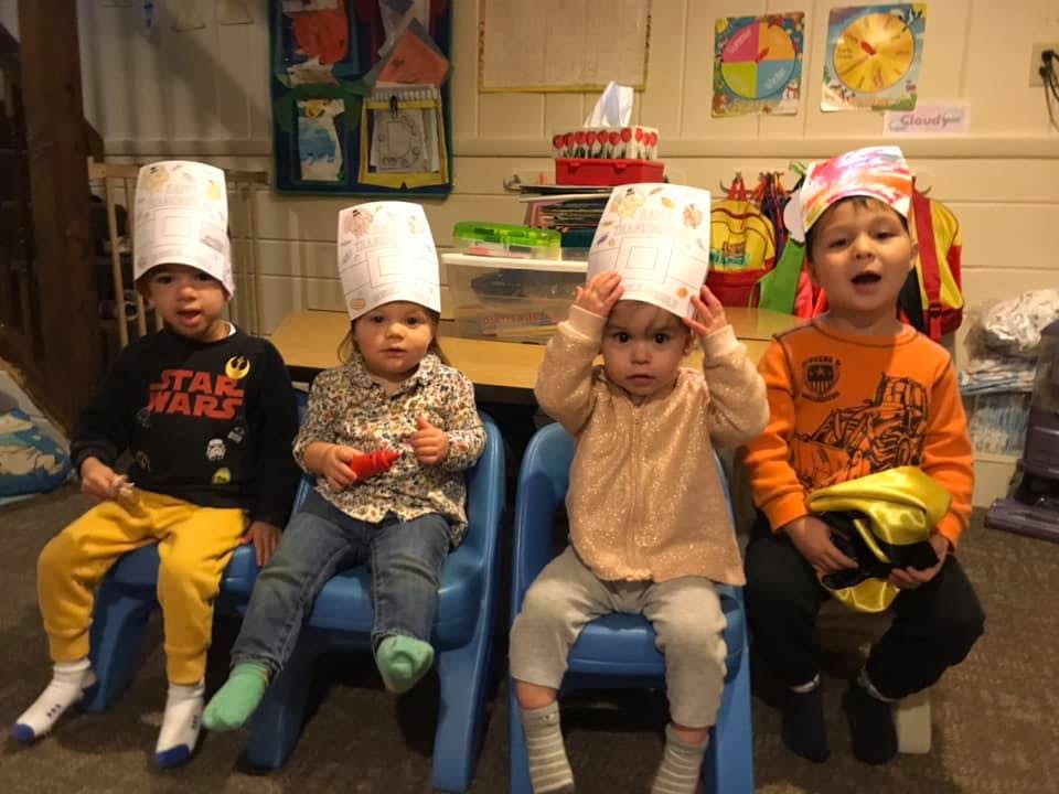 Four children wearing paper hats sitting in chairs