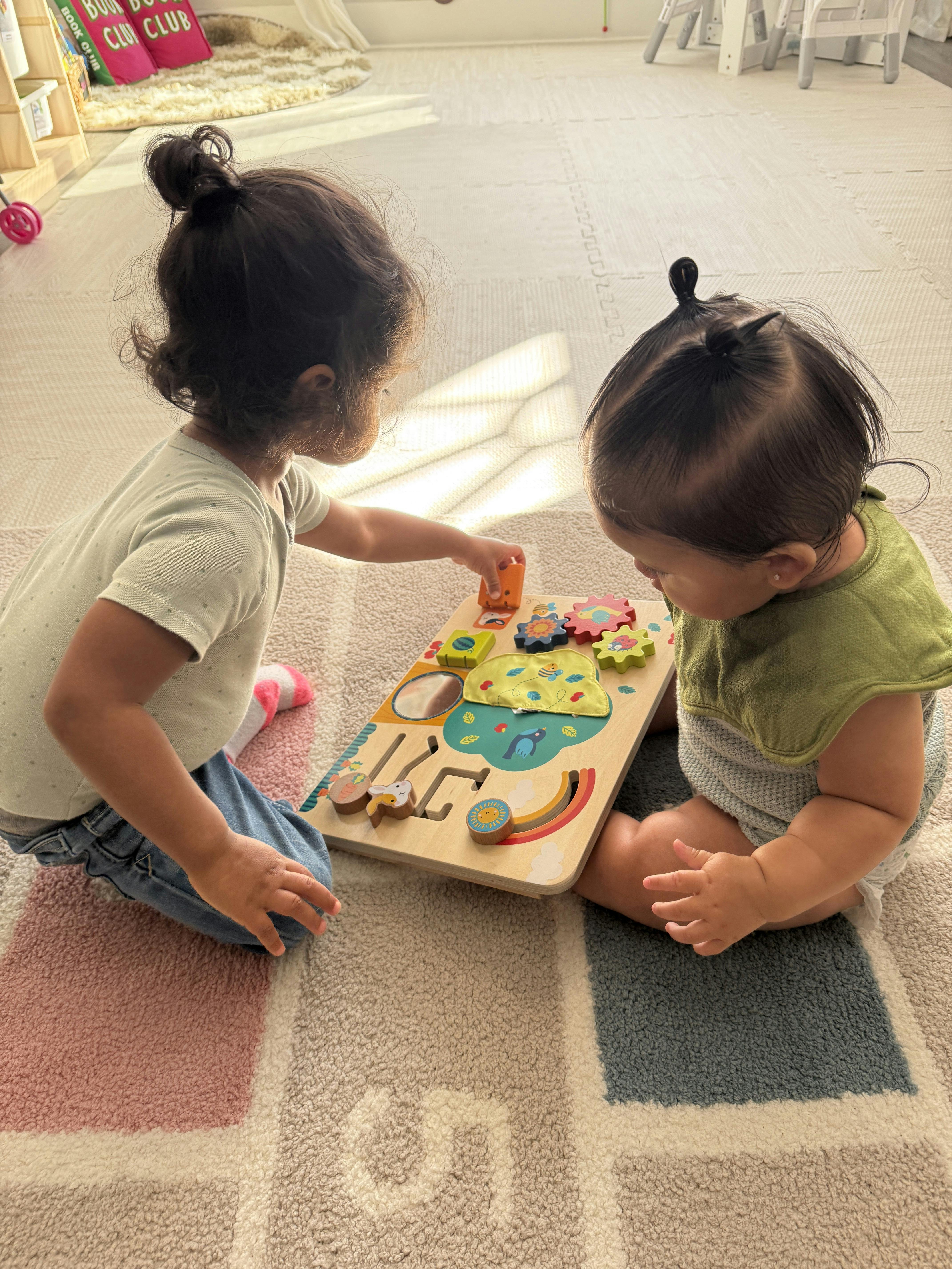 Two children sitting on a mat playing with a wooden activity board
