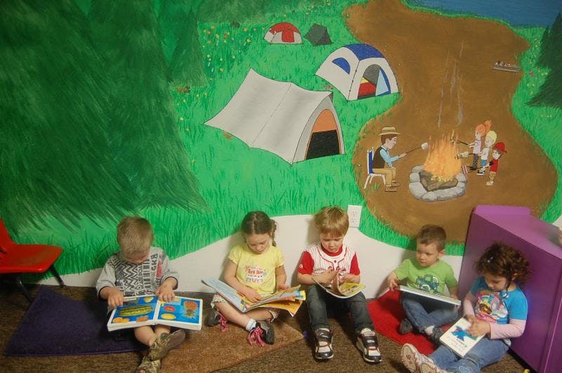 Five children sitting on the floor reading books in a classroom