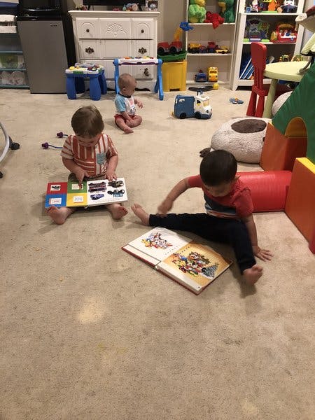 Three children sitting on the floor with books and toys