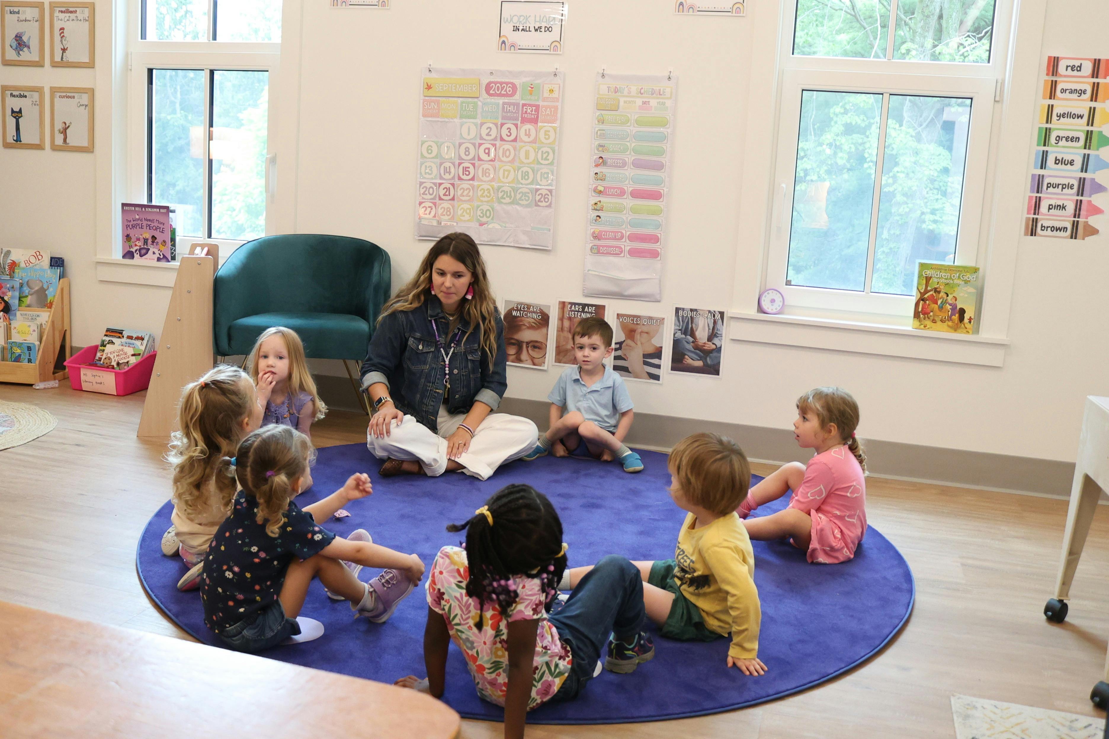 Teacher and children sitting in a circle on a rug in a classroom