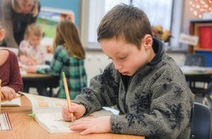 Child writing in a notebook at a desk in a classroom