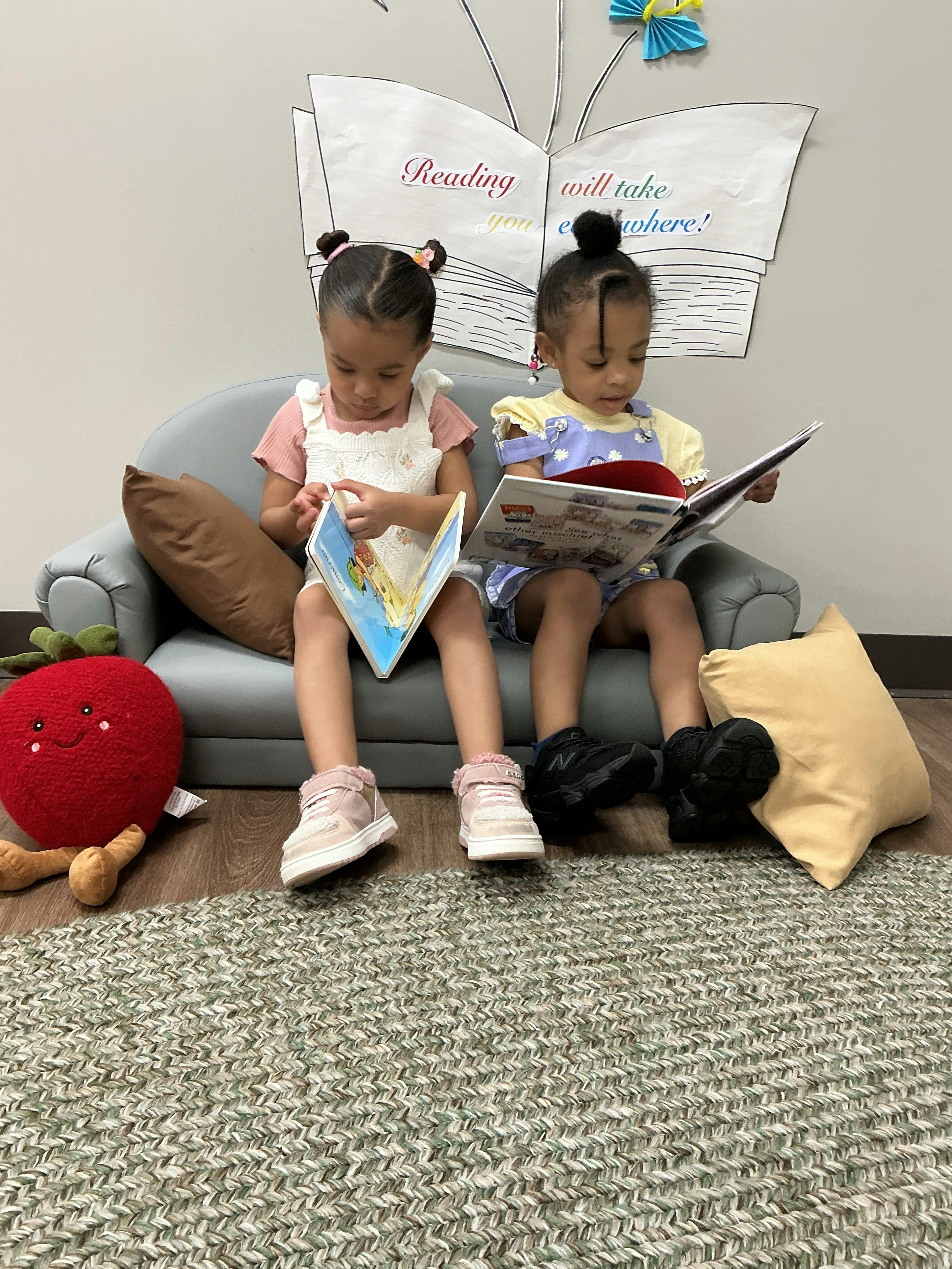 Two children sitting on a small couch, reading books
