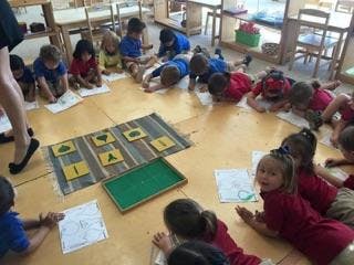 Children sitting on the floor in a classroom with a person standing